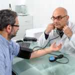 Stressed worker at a desk with elevated blood pressure monitor, representing occupations with the highest hypertension risk