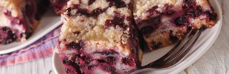 Slice of blueberry coffee cake with homemade blueberry pie filling and simple glaze on a white background