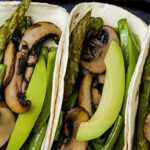 Grilled asparagus shiitake tacos topped with guacamole and lime on corn tortillas