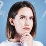 Pensive young woman with short hair looking thoughtful, surrounded by floating question marks on a blue background.