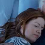 Couple sleeping together in bed, with a woman resting her head on her partner’s chest as they lie under white bedding at night.