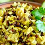 A rustic wooden bowl filled with Lebanese mujadara made of lentils and yellow rice, garnished with fresh parsley, surrounded by cucumbers, raw rice, and lentils on a wooden table.