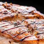 Grilled sea bass on a wooden board garnished with lemon slices and herbs, seasoned with spices.