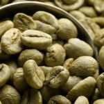 Close-up of raw green coffee beans in a burlap sack with a metal scoop.