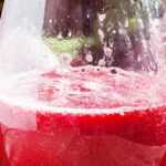 Glass of fresh beetroot juice with whole and sliced beets and leafy greens on a rustic wooden table.