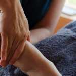 Close-up of a person receiving a reflexology foot massage, with hands applying pressure to the sole while the client relaxes on a towel-covered surface.