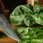 hands holding a knife and chopping spinach