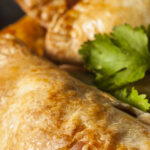 Golden-brown baked picadillo pockets with flaky crust, garnished with fresh cilantro and served alongside a small bowl of salsa.