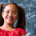 smart girl writing mathematical problems on chalk board