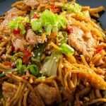 A bowl of stir-fried noodles with vegetables and chicken