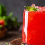 Refreshing watermelon juice served in a glass with ice and mint, placed on a wooden board alongside fresh watermelon slices and a halved lime.