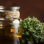 Glass jar filled with thyme oil beside fresh thyme sprigs and a mortar and pestle.