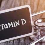 Stethoscope resting on a wooden surface next to a small chalkboard labeled “Vitamin D,” representing vitamin D and health care concepts.