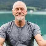 senior man meditating by a lake