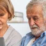 Worried senior couple sitting on a sofa, looking at a laptop screen together while reviewing health or financial information at home.