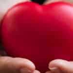 Hands gently holding a red heart symbol, representing heart health and care.