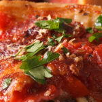 Slice of Chicago-style deep-dish pizza layered with spinach, artichokes, mushrooms, melted cheese, and chunky tomato sauce, garnished with fresh parsley on a plate.
